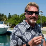 Tech entrepreneur John McAfee smiling at a public tech conference, representing the foundation of his career.