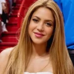 A high-quality portrait of Colombian singer Shakira, sister of Patricia Mebarak, smiling at a sports stadium.