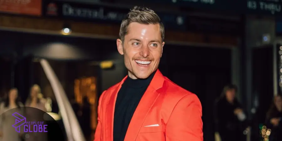 A professional portrait of Sawyer Hemsley smiling in a vibrant orange blazer at a formal event.