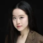 A professional headshot of Stephanie Soo in a brown blazer against a dark background.
