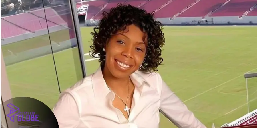 A portrait photo of Jamiko Vaughn smiling warmly in a white button-down shirt with a cross necklace, set against a stadium backdrop.